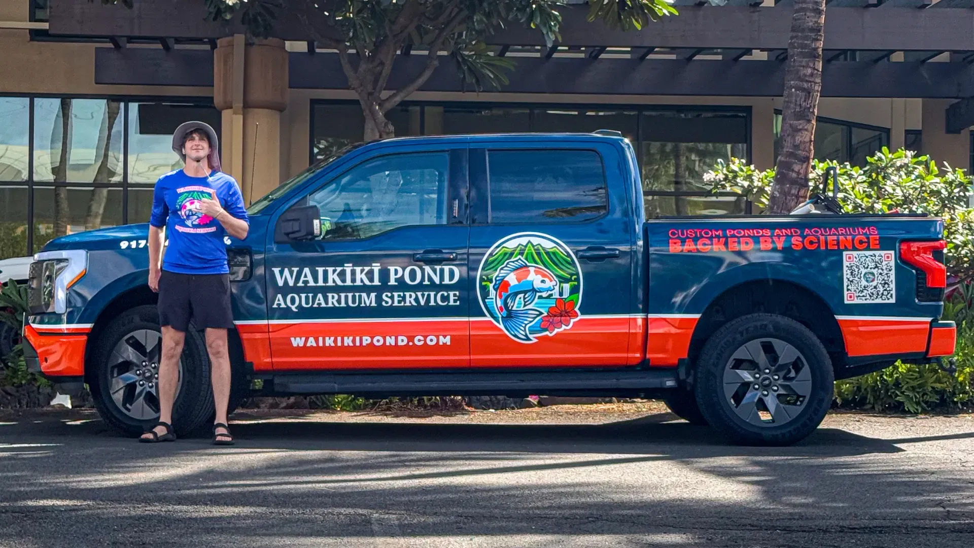 The wrapped F-150 Lightning in side profile with the owner beside it in a branded shirt: koi badge on the door, the name and waikikipond.com along the body, and a QR code on the bed.